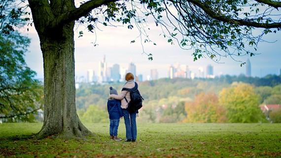 Bestemor og barnebarn står på en høyde og ser utover grønne parker og skyskrapere